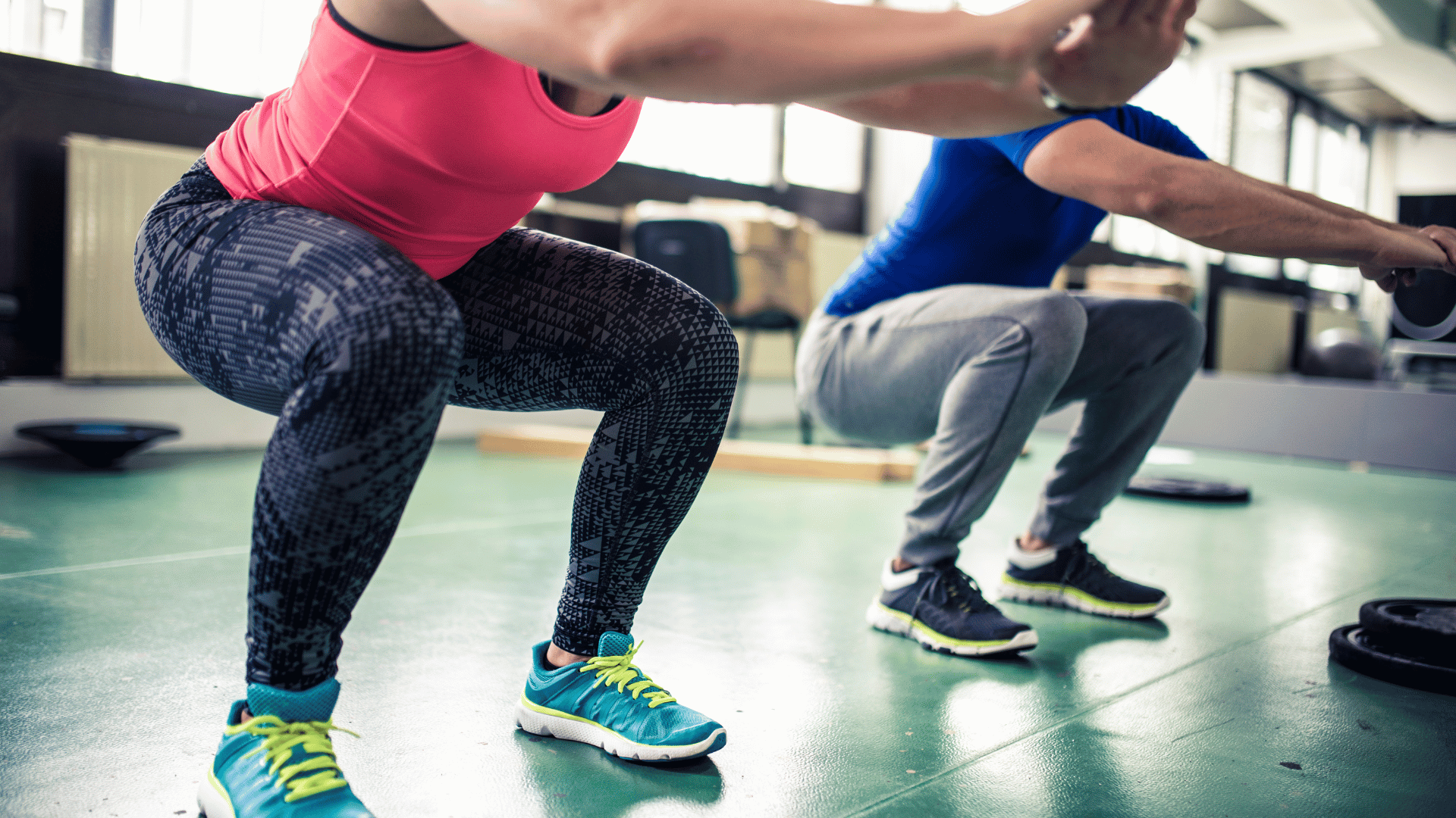 Two people performing air squats in a gym, focusing on proper form and leg alignment.