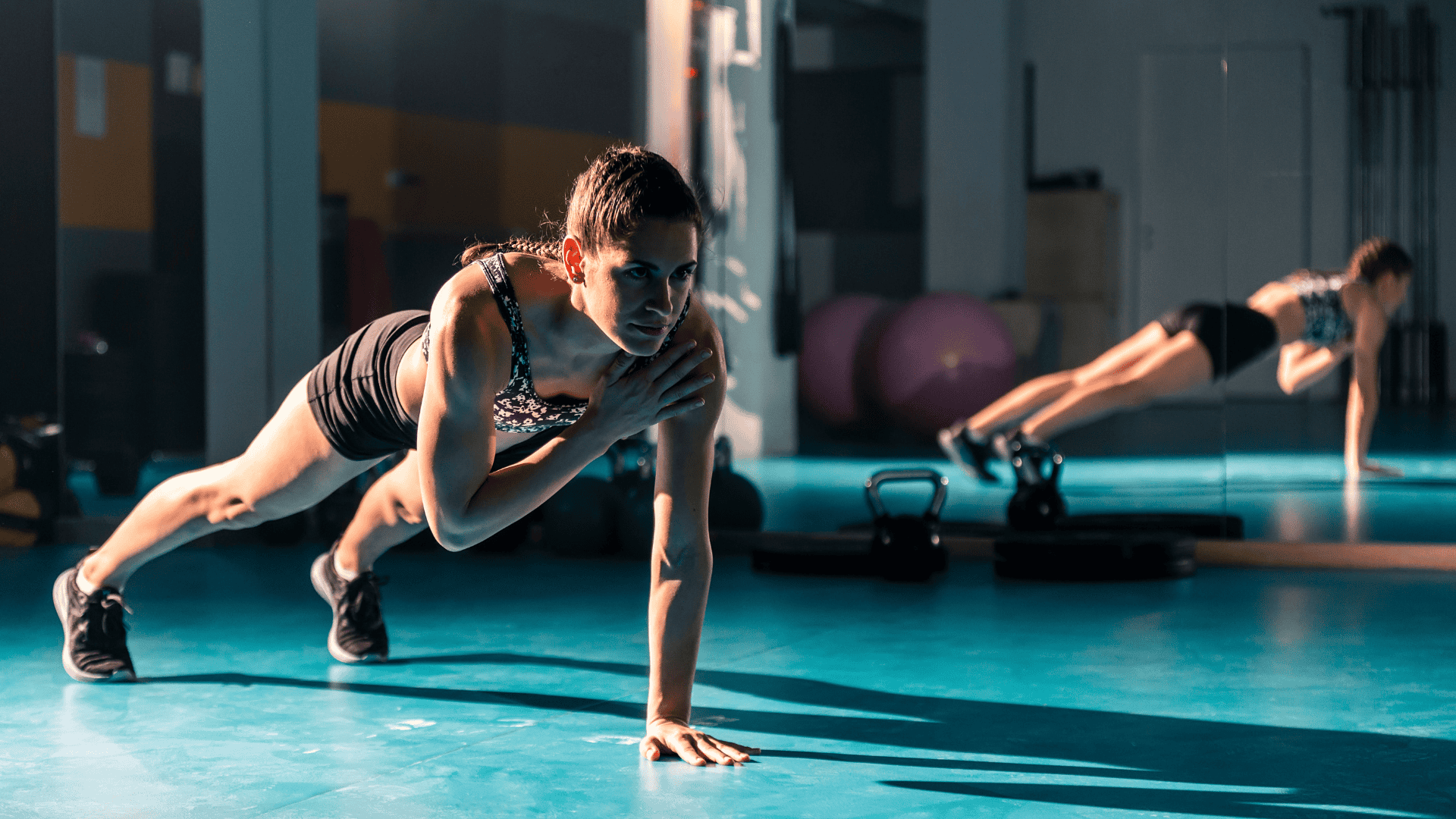 A young female doing a Pilates plank shoulder taps in the gym