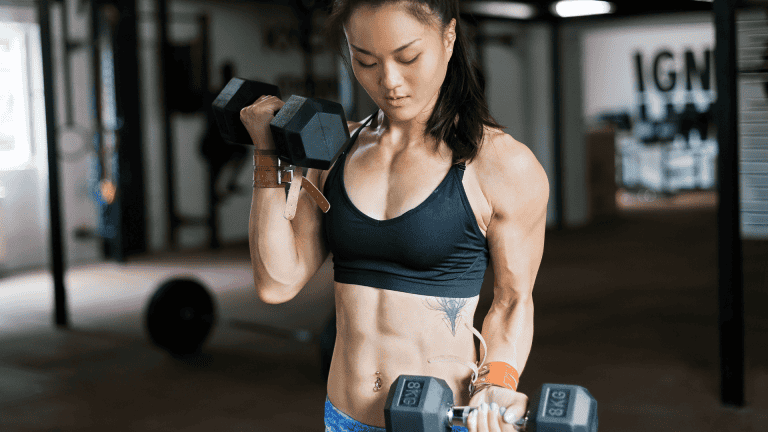 Woman performing bicep curls with dumbbells in a gym.