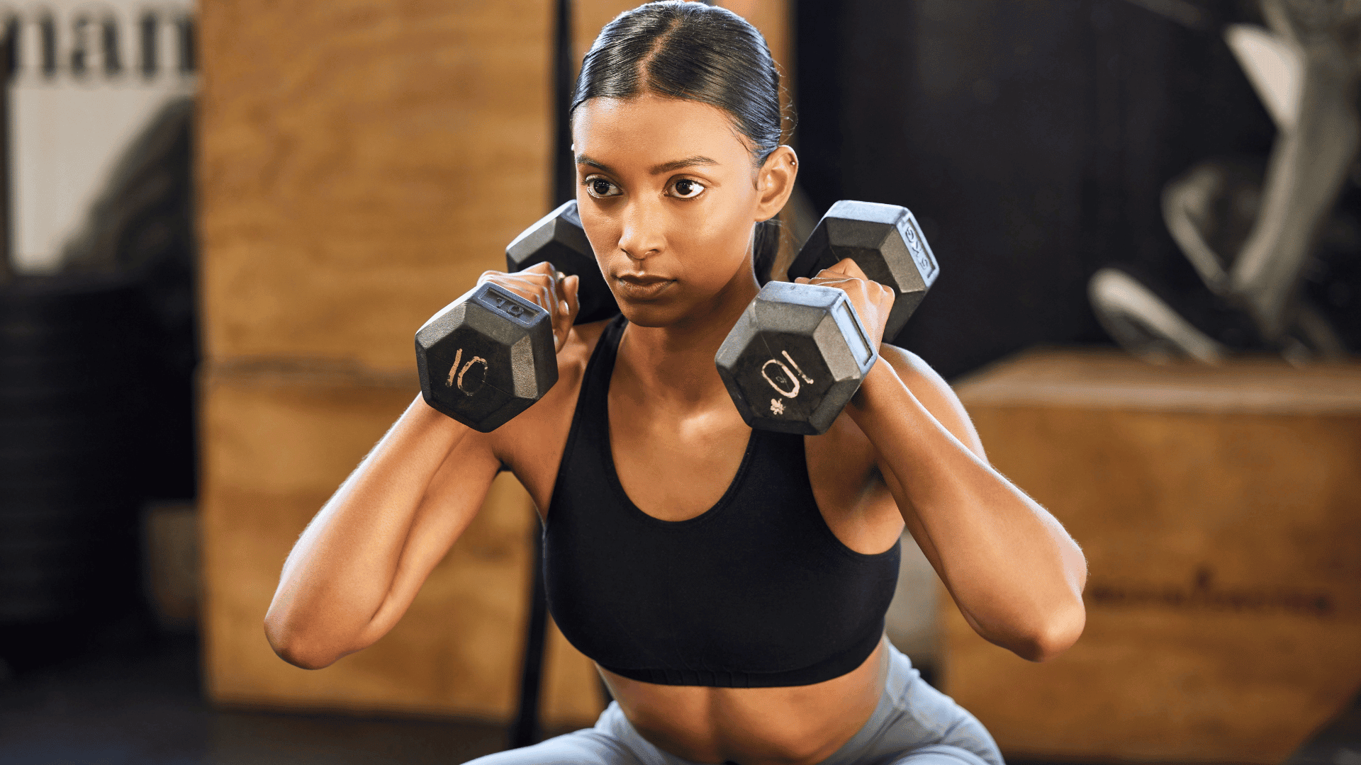 Woman doing dumbbell squats in a gym, focused on form.