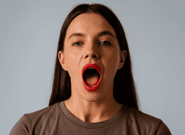 Woman with mouth open wide, demonstrating a jaw release exercise for facial relaxation.