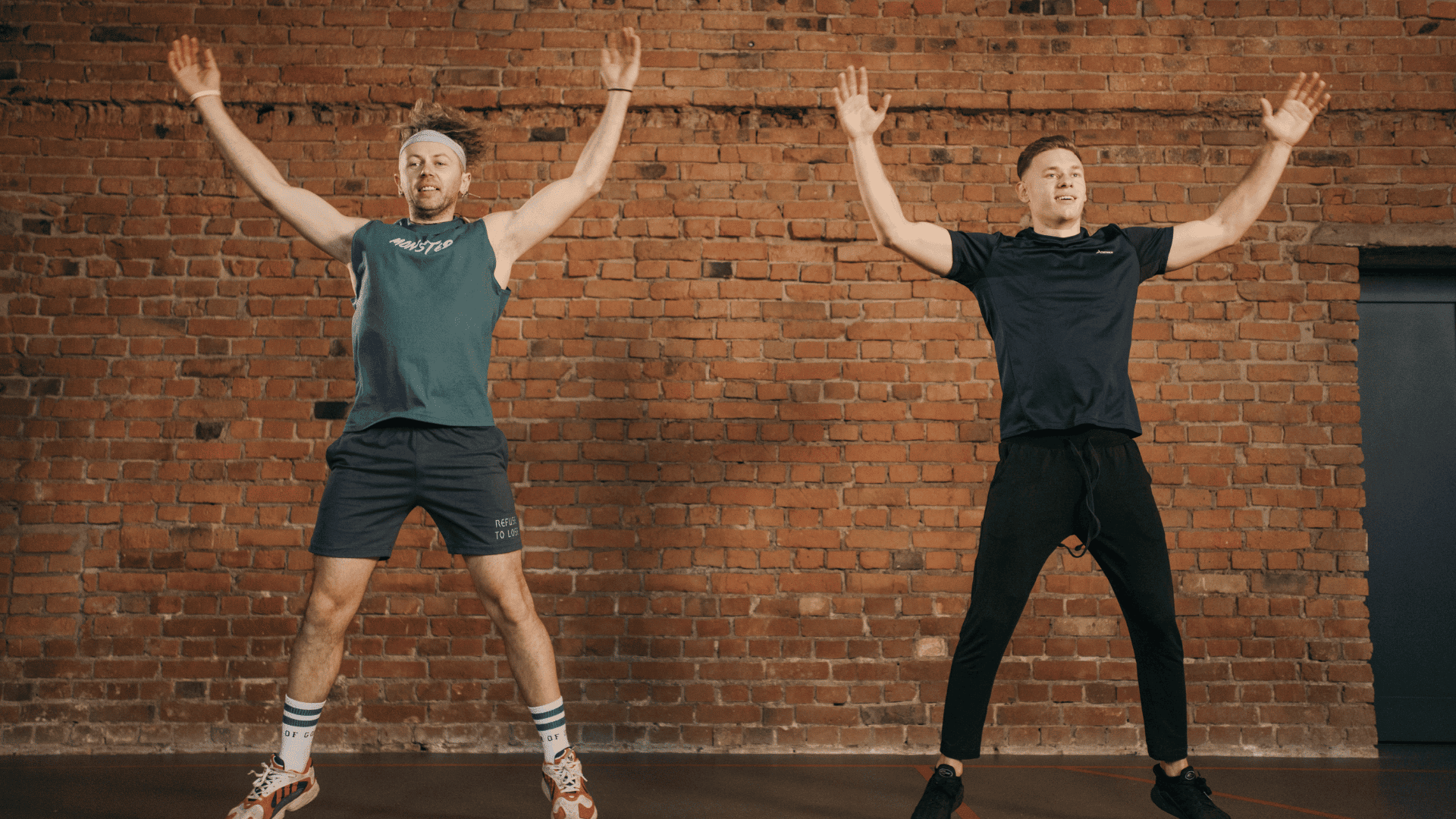 Two men doing jumping jacks in a gym.