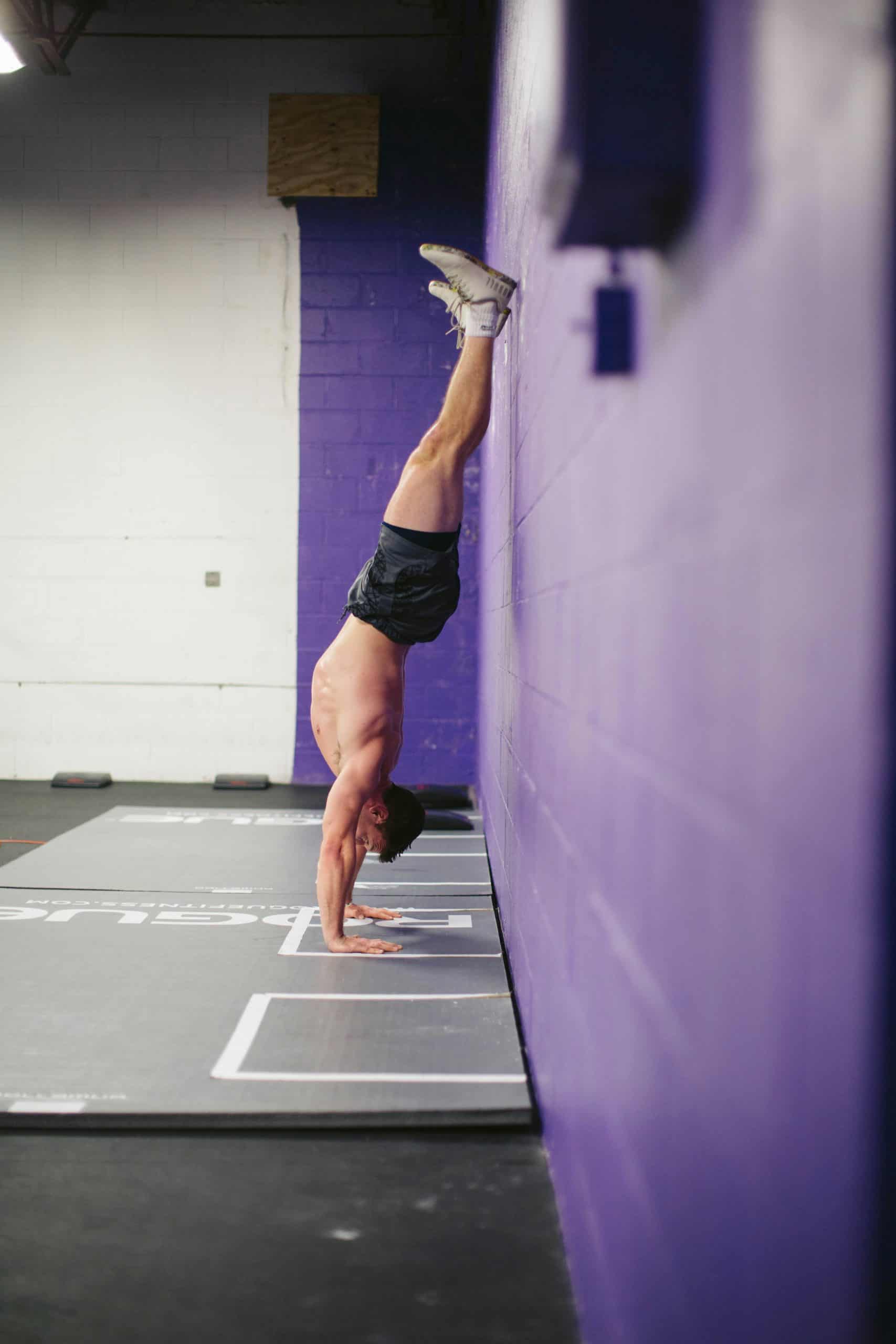 mariah-krafft-fepcZPBGkv4-unsplash "Man performing a handstand against a purple gym wall during a wall Pilates or strength training session.
