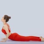 Young woman in red activewear performing a gentle back extension pose on the floor, demonstrating Somatic Pilates practice