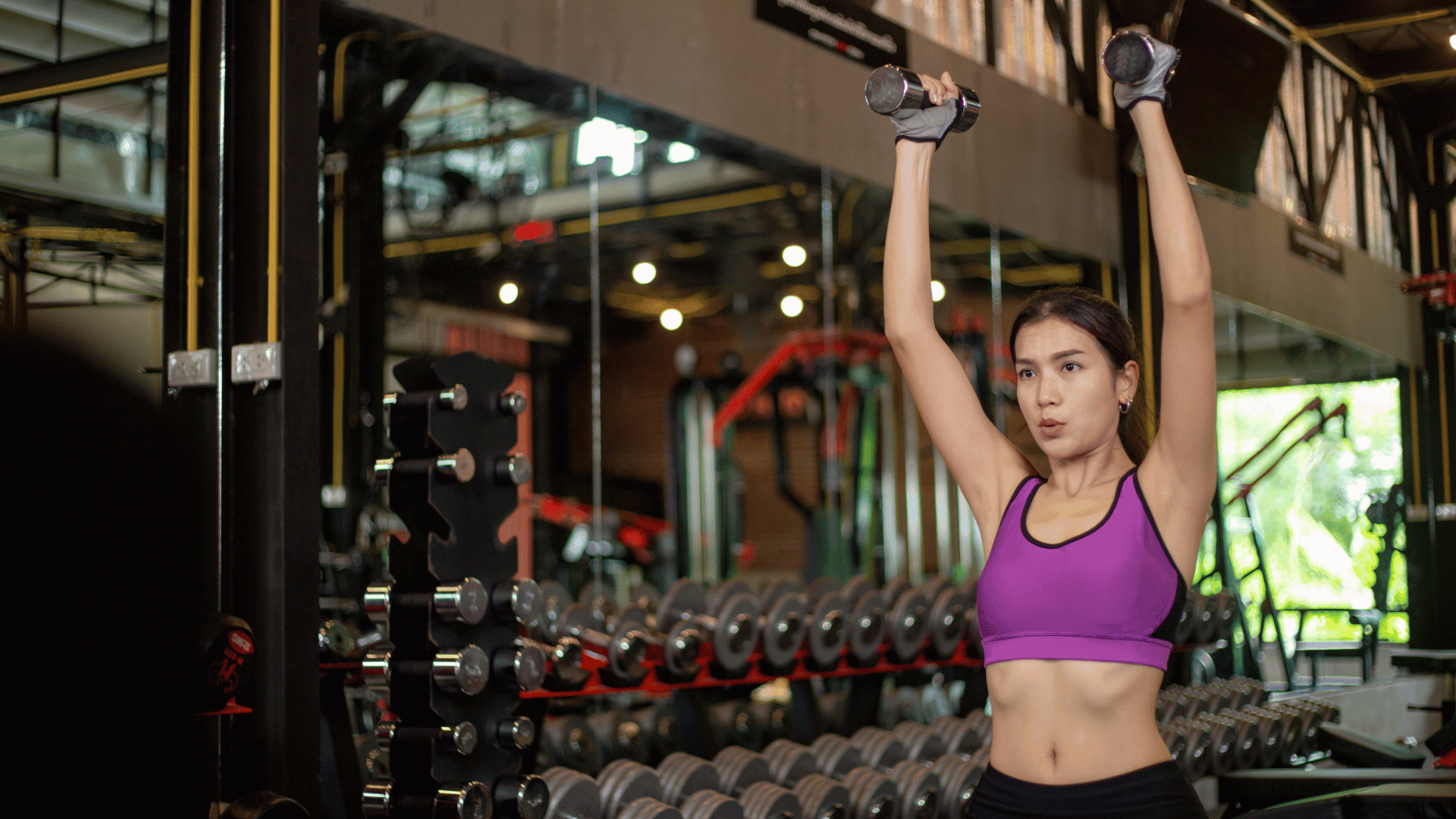 AN Overlay Template - 2025-08-05T160021.995 Woman performing an overhead dumbbell press in a gym, showcasing upper body strength training with a focus on hammer curls and cardio.