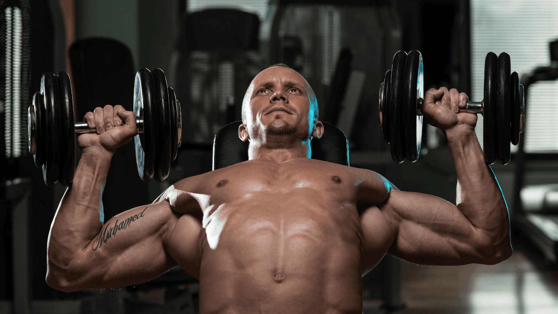 Focused man performing a dumbbell chest press in a gym, demonstrating strength training progression — symbolizing consistency and intensity as key factors for weekly workout improvements.