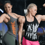 Two muscular women flexing their arms confidently in a gym, symbolizing the results of a 12-week strength training program designed to build curves and empower women.
