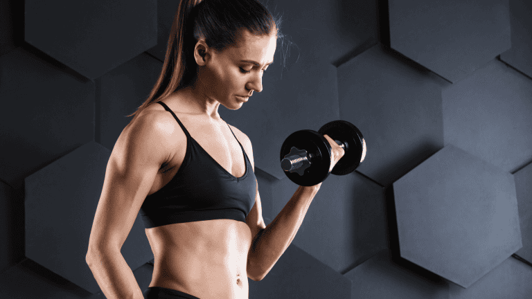 Fit woman in black activewear doing a dumbbell bicep curl against a stylish hexagonal wall. Promotes a 4-day workout plan designed for women focused on toning up or burning fat.
