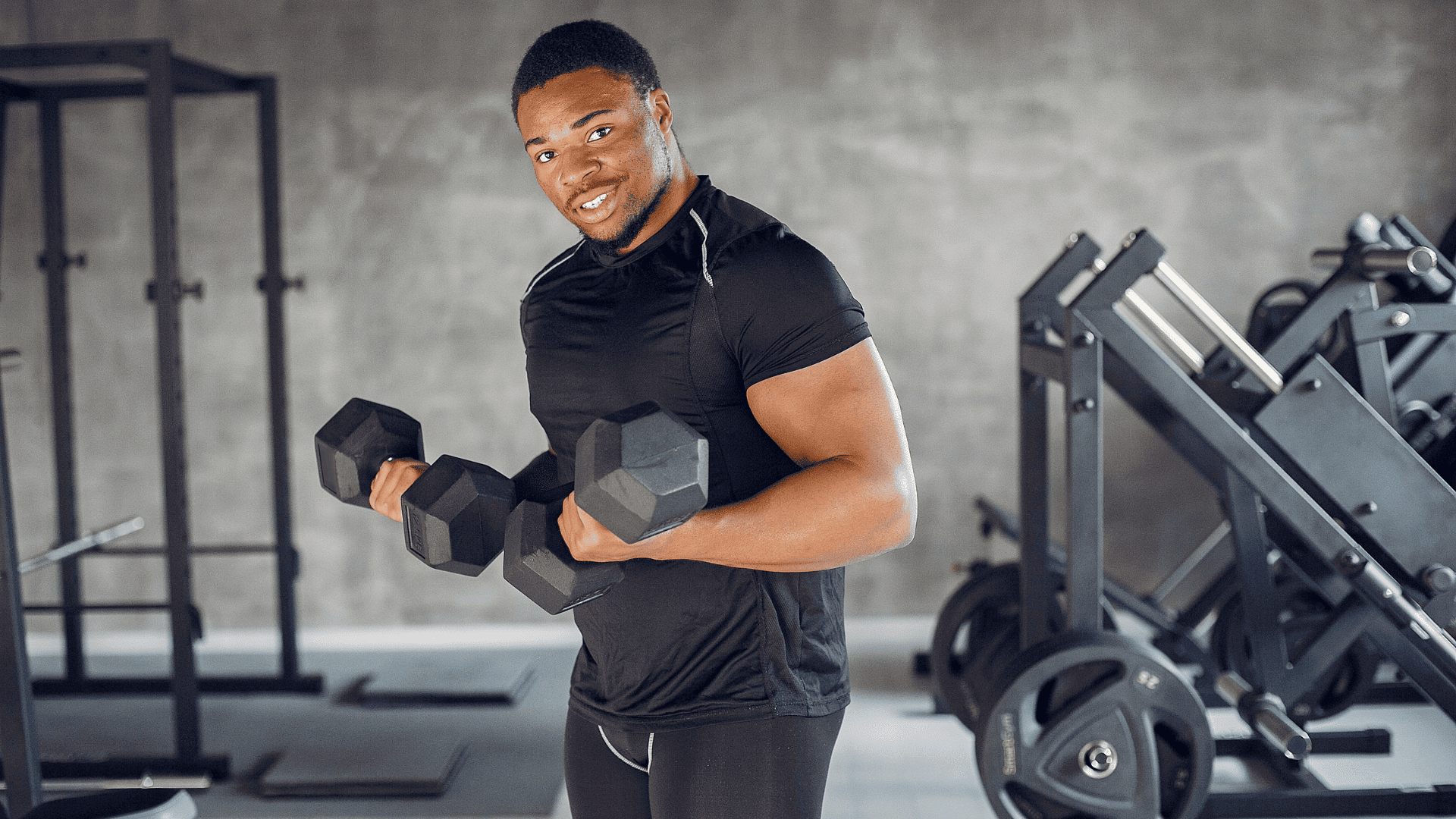 Man lifting dumbbells and smiling at the gym, representing Planet Fitness as a welcoming and effective place to begin a fitness journey.        Ask ChatGPT