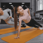 Teenage girl doing plank exercise at the gym, working out with personal trainer