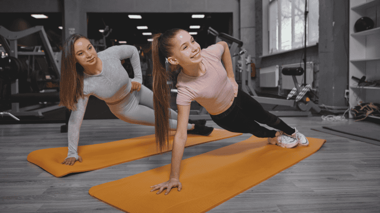 Teenage girl doing plank exercise at the gym, working out with personal trainer