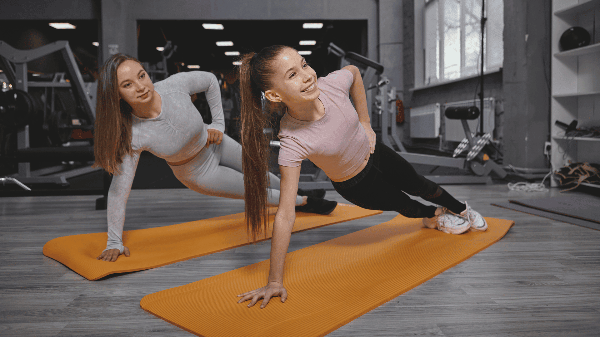 Teenage girl doing plank exercise at the gym, working out with personal trainer
