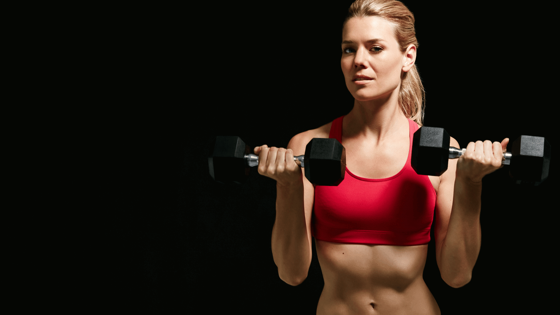 Woman in red sports bra lifting dumbbells with focused expression, illustrating a common workout mistake of rushing through reps during core training.