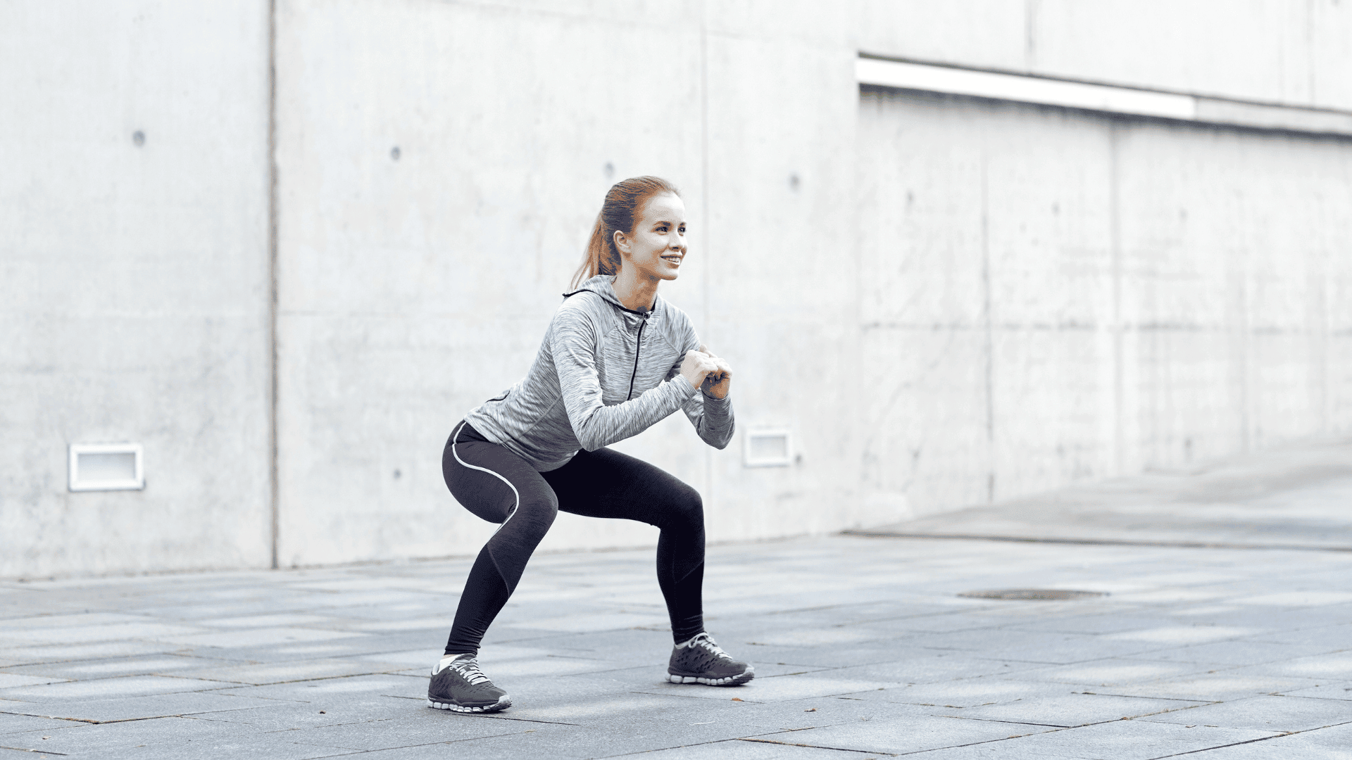 Smiling woman performing bodyweight squats outdoors in athletic wear.