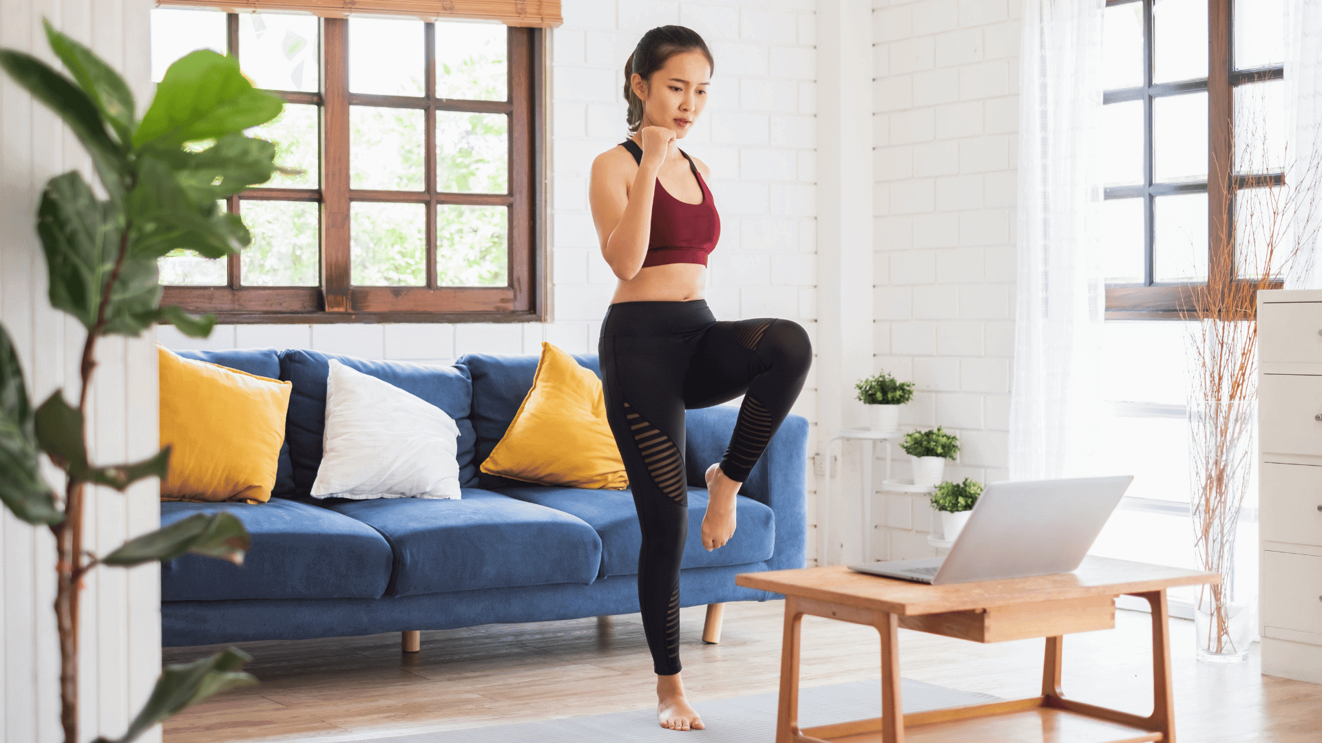 Woman doing a virtual step workout at home, raising her knee with focus and control.