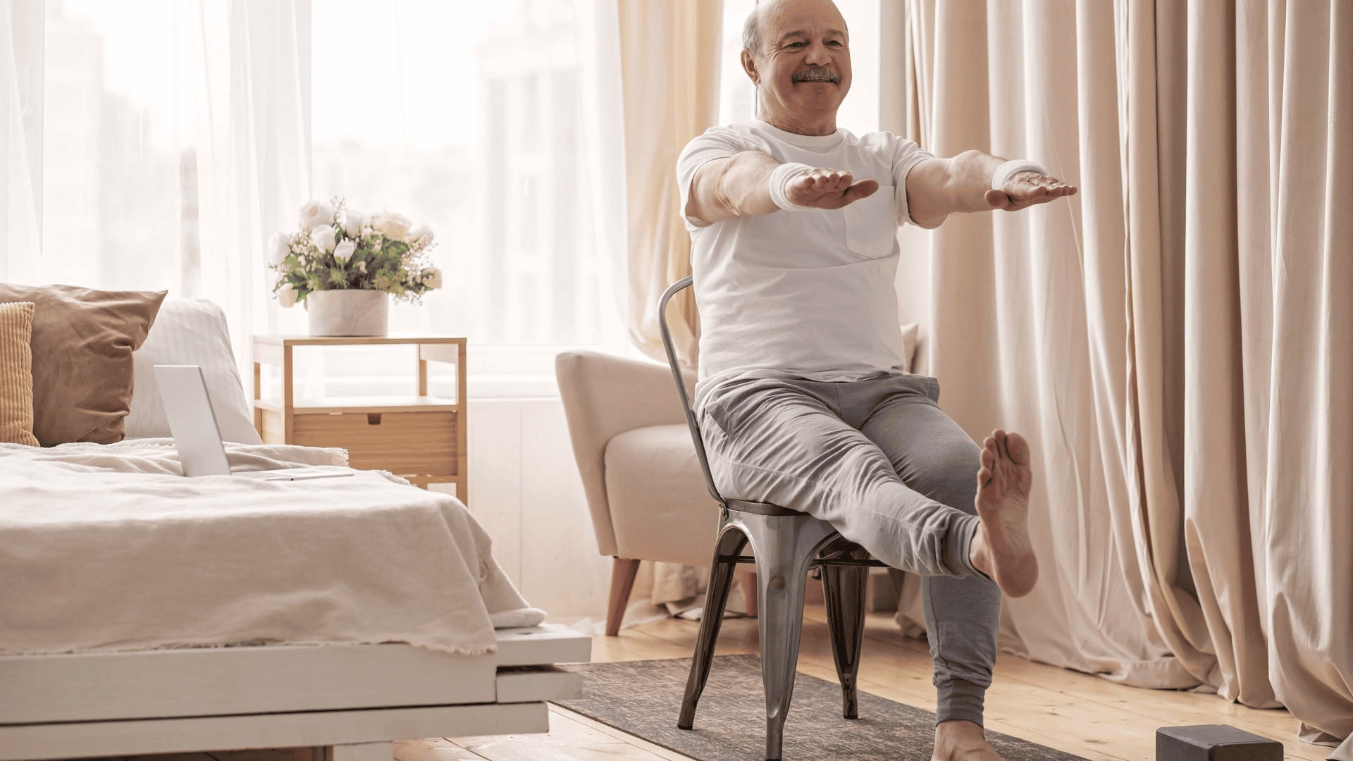 man sitting on a chair at home, lifting one leg and extending both arms forward, practicing arm and leg coordination exercises.