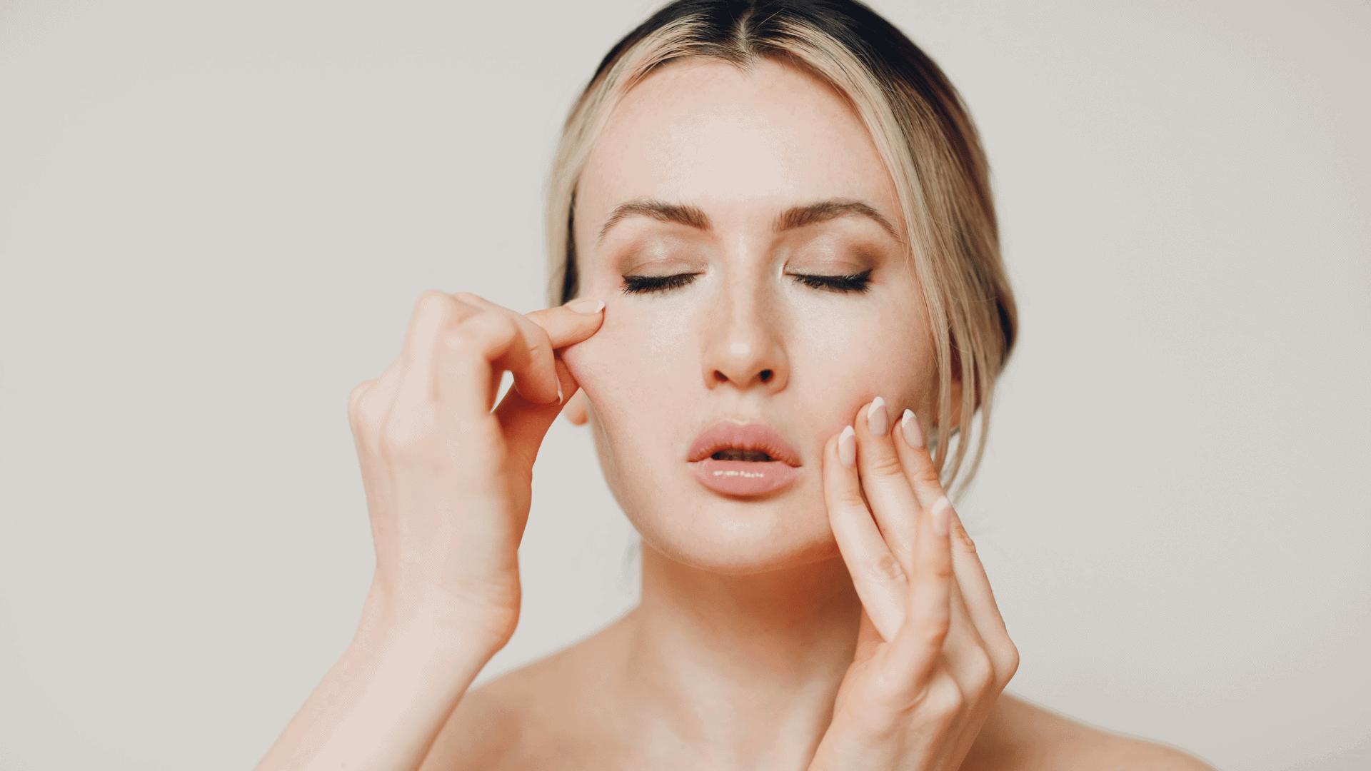 Woman performing a face yoga exercise by gently pinching her cheeks with eyes closed.