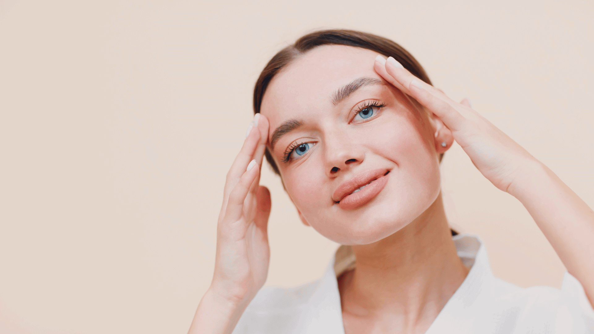 Woman performing an upper eyelid face yoga exercise with hands placed near temples.