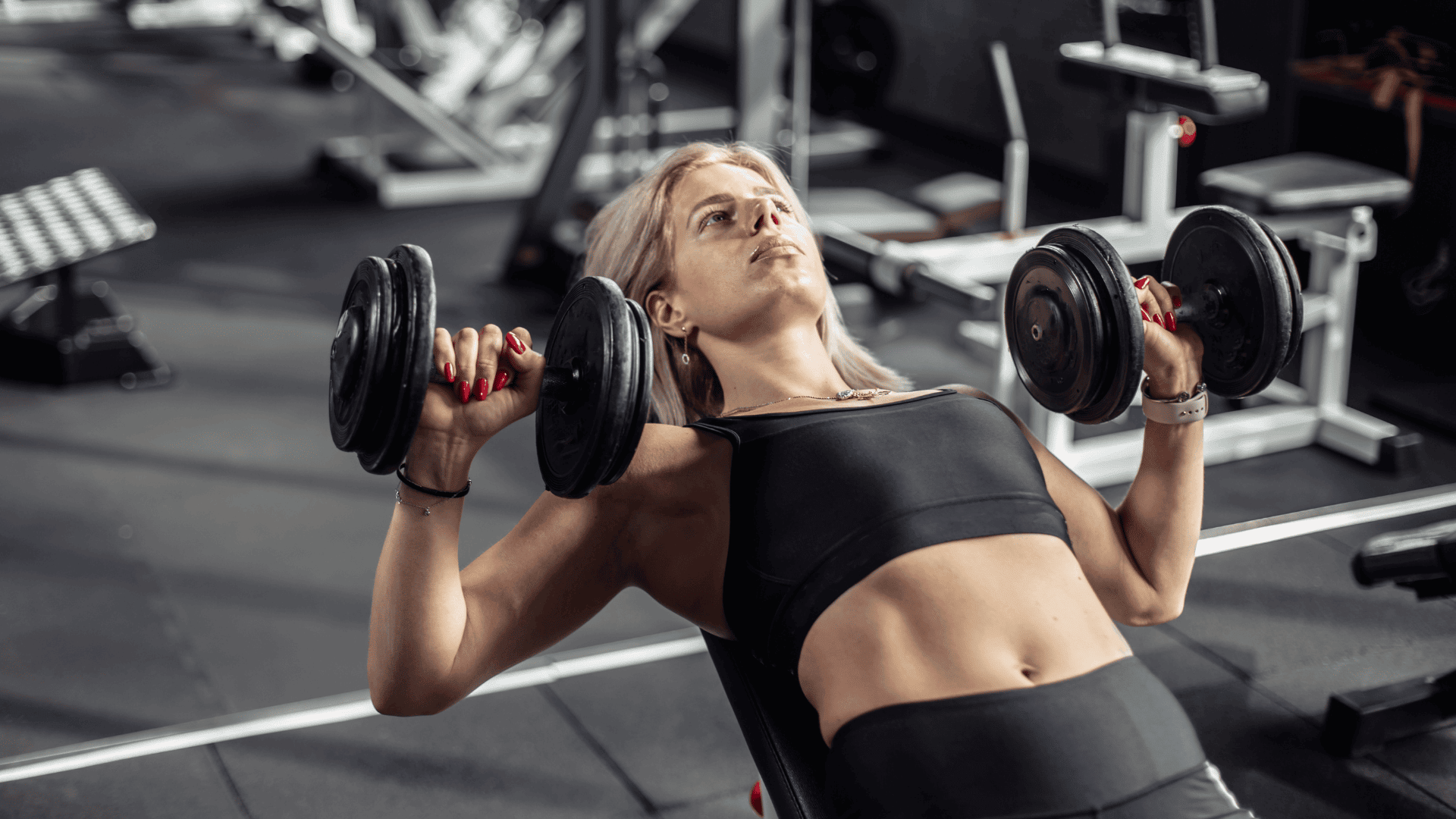Fit woman performing a dumbbell chest press on an incline bench at the gym.