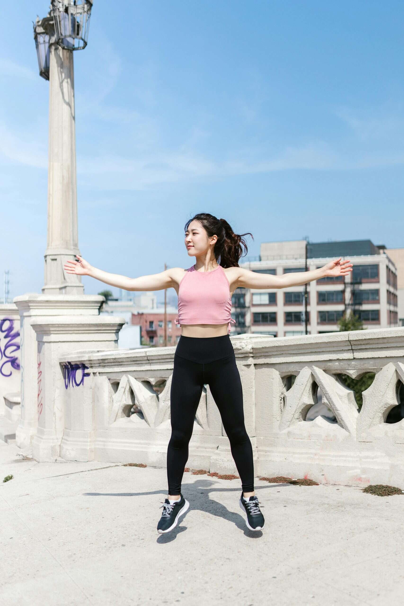 Woman performing jumping jacks outdoors as part of a high-rep cardio workout.